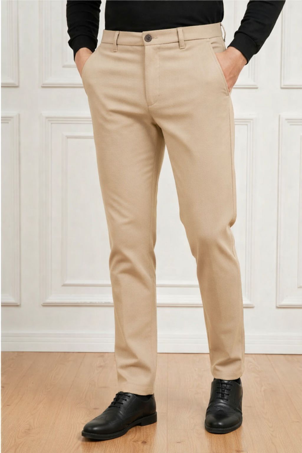 Person wearing beige pants and black shoes against a white paneled wall.