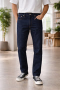 Person wearing dark blue jeans and black sneakers in a room with plants and furniture.